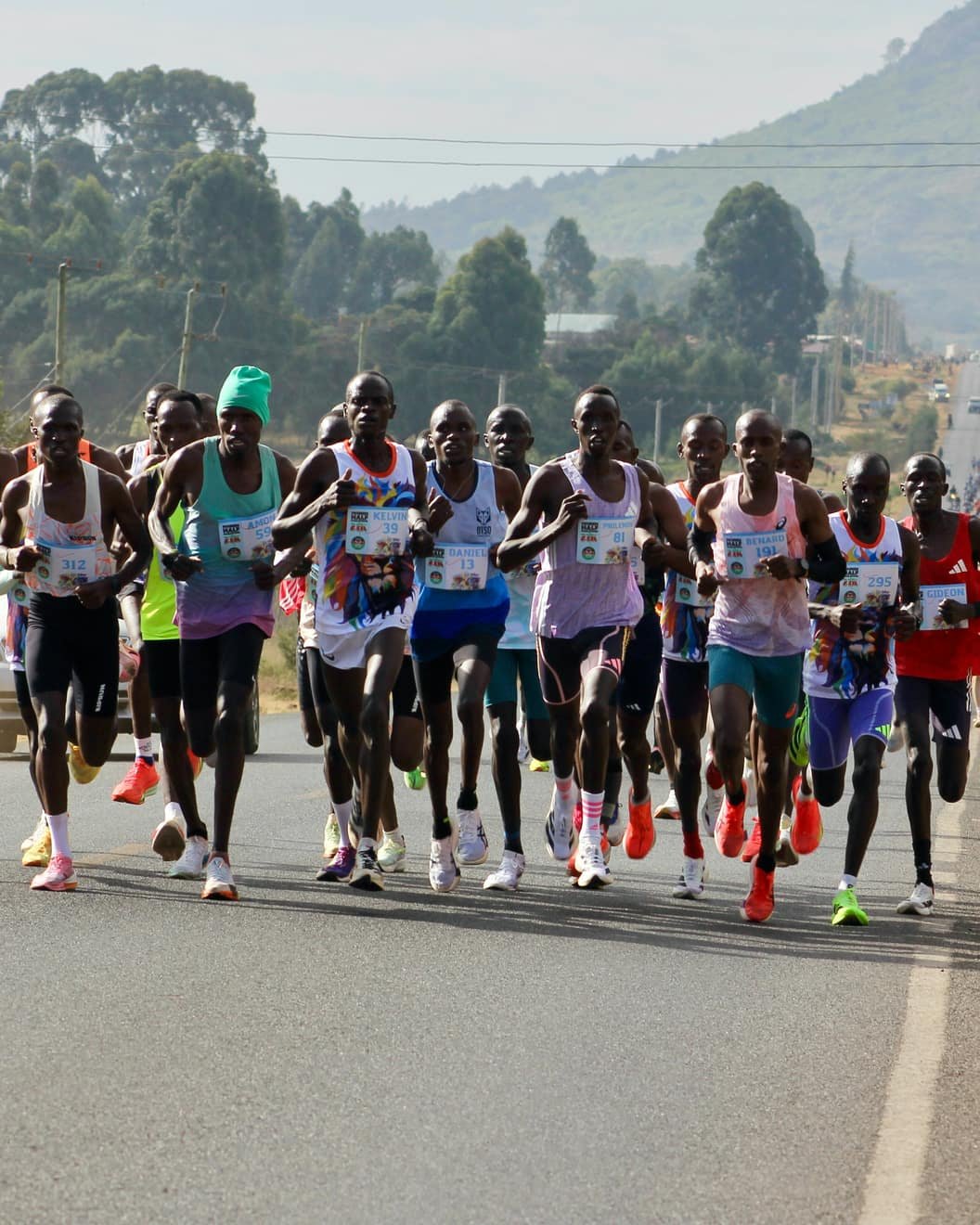 Peloton de coureurs de fond lancé sur une route des hauts plateaux de la Rift Valley, au Kenya, une colline en toile de fond.